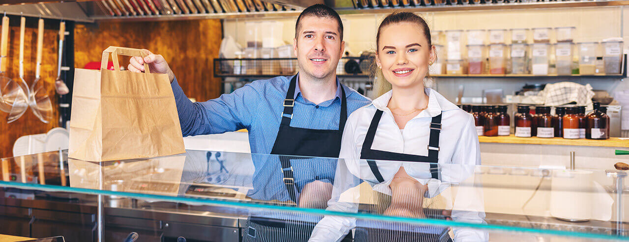 Man and woman at restaurant/deli counter handing over a food bag