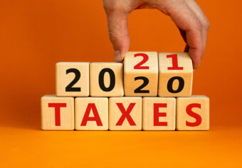 Business concept of planning 2021. Male hand flips wooden cubes and changes the inscription 'Taxes 2020' to 'Taxes 2021'. Beautiful orange background, copy space.