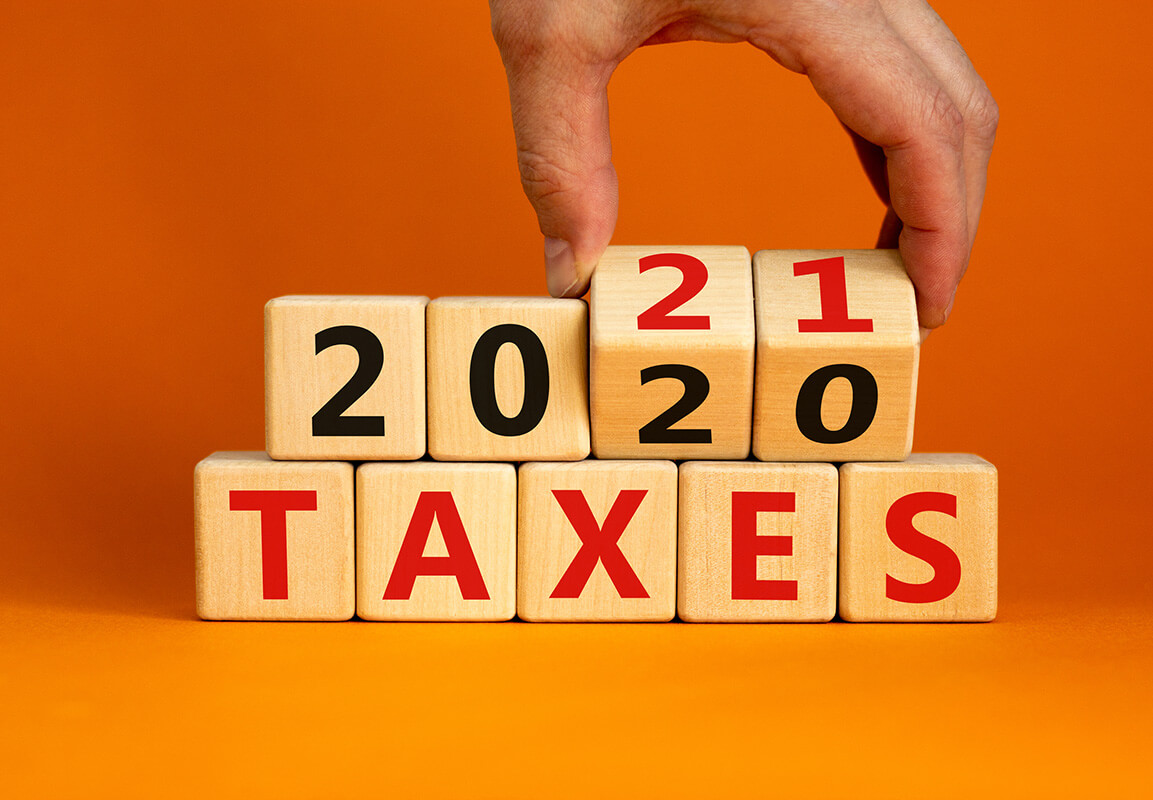 Business concept of planning 2021. Male hand flips wooden cubes and changes the inscription 'Taxes 2020' to 'Taxes 2021'. Beautiful orange background, copy space.